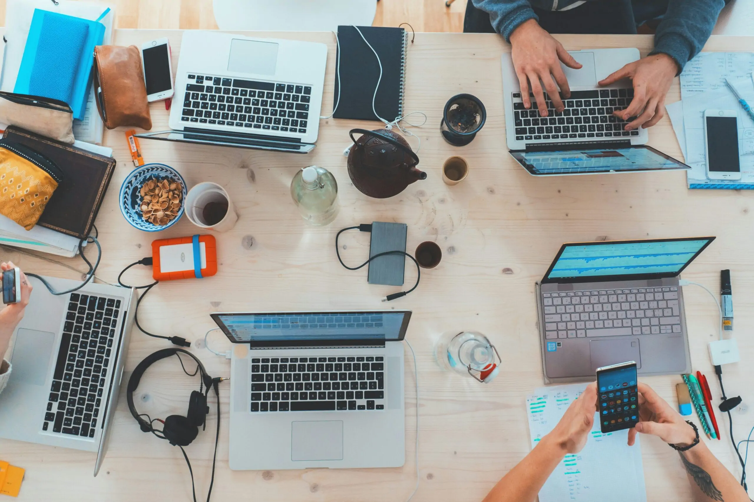 Team of people collaborating with laptops, smartphones, and digital tools at a shared workspace, symbolizing entrepreneurial teamwork and website development.